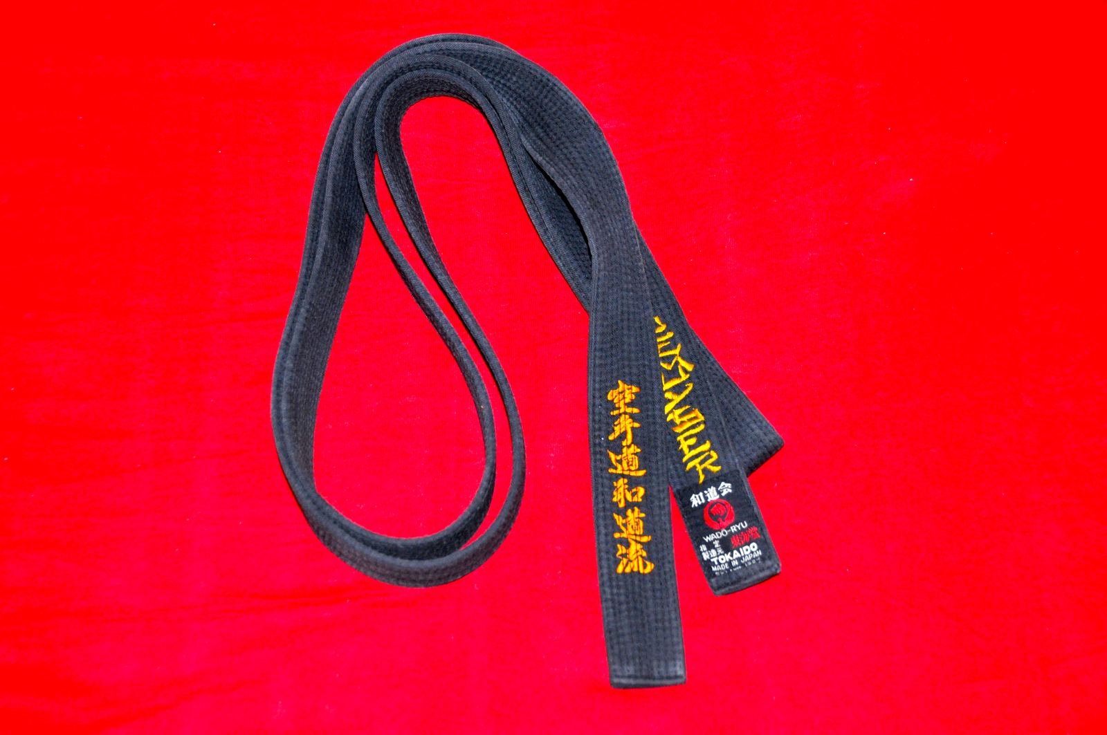 A black karate belt with gold embroidered lettering on a red background